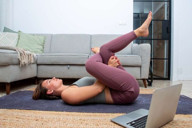 Une femme fait des étirements au sol chez elle avec un ordinateur pour reprendre le sport