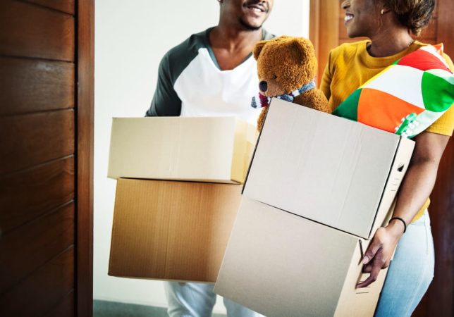 Un couple souriant portant des cartons de déménagement en Martinique en entrant dans leur nouveau logement