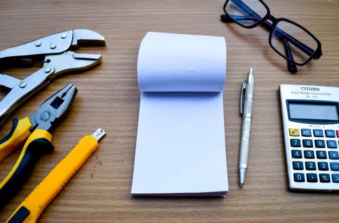 Outils de plomberie, bloc-notes vierge, stylo et calculatrice sur un bureau en bois, prêts pour la facture de plombier.