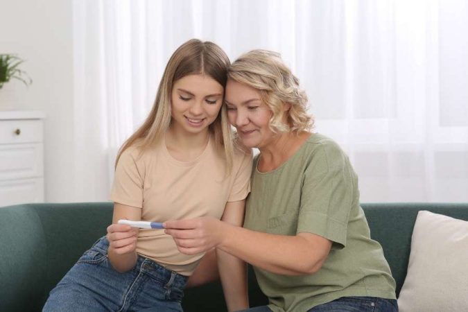 Annoncer sa grossesse : une jeune femme montre un test de grossesse positif à sa mère émue.