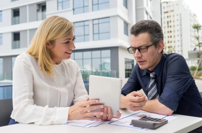 Une agente immobilière et un propriétaire consultent une tablette pour un bien immobilier surestimé baisser prix.