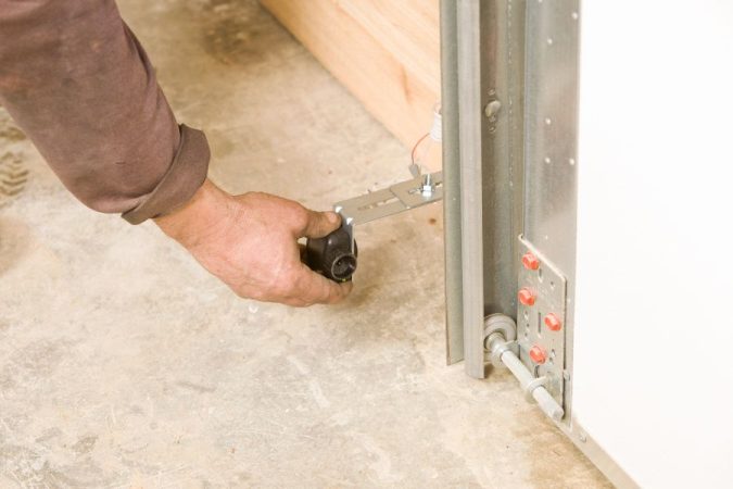 Gros plan sur la fixation basse d'un rail de porte de garage, montrant l'intervention nécessaire pour ajuster une porte qui frotte contre le sol.